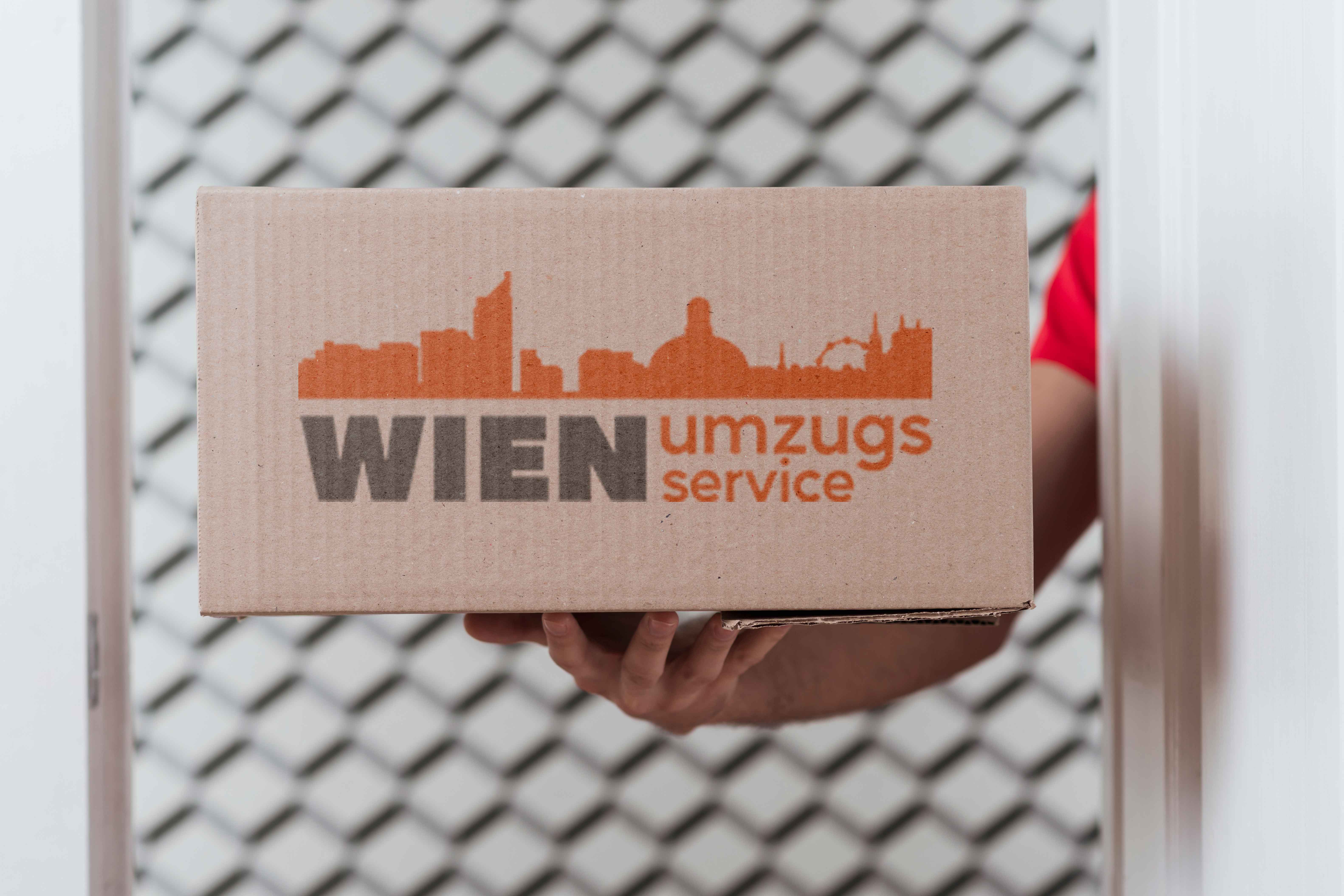 Ein Mann hält in der rechten Hand eine Kiste mit der Aufschrift 'Wien Umzugsservice'