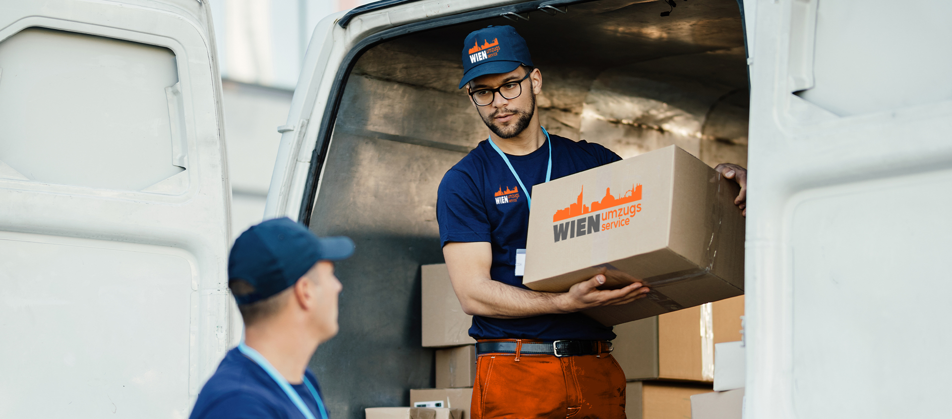 Zwei Arbeiter bringen Kisten mit der Aufschrift 'Wien umzugsservice' in den Transporter.